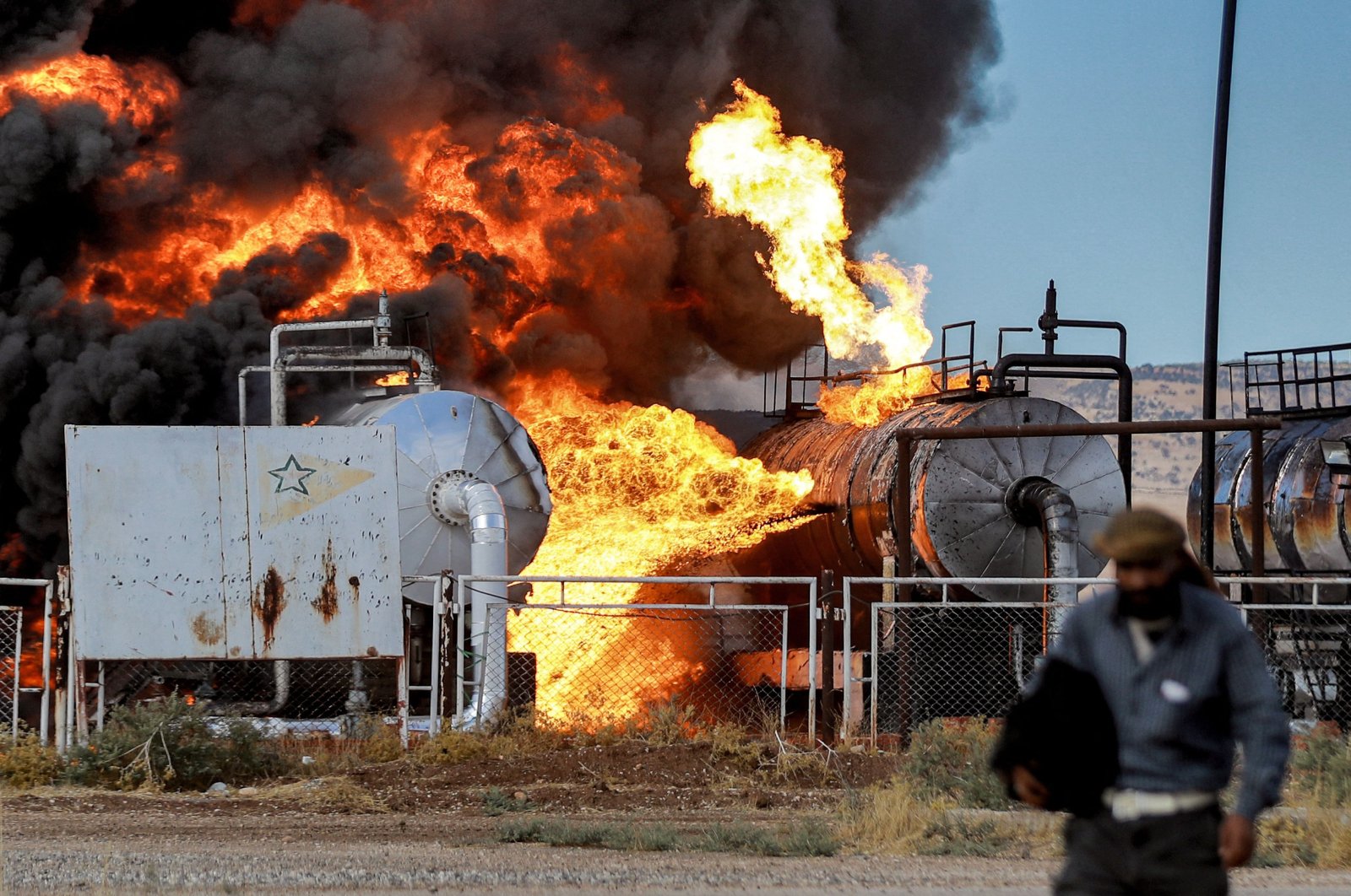 A man walks close to a fire raging at the Zarba oil facility run by the PKK/YPGterrorist group after a reported Turkish airstrike, al-Qahtaniyah, Syria, Oct. 5, 2023. (AFP Photo)