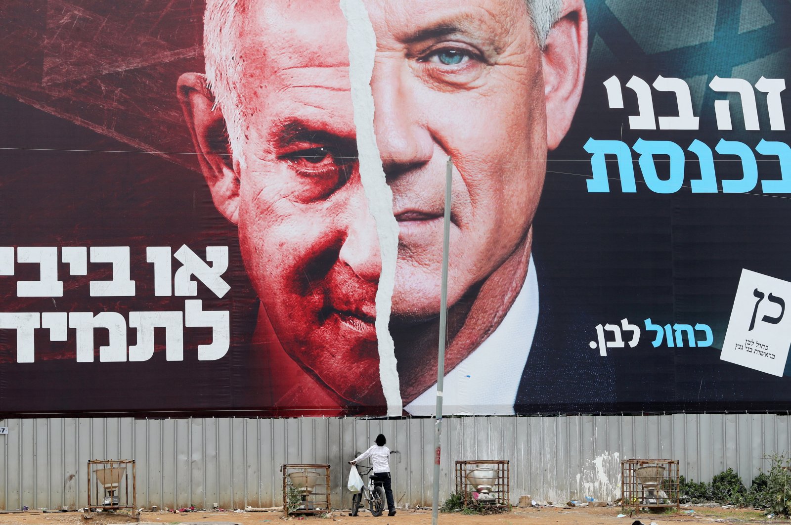 A boy looks up at a Blue and White party election campaign banner depicting its leader, former Israeli Defense Minister Benny Gantz, alongside Israeli Prime Minister Benjamin Netanyahu, ahead of the March 23 ballot, Bnei Brak, Israel March 22, 2021. (Reuters File Photo)
