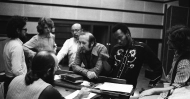 American jazz musician Herbie Mann (1930-2003) leans on a piano (C) at a recording studio with Mick Taylor, Ahmet Ertegün and Albert Lee, among others, 1973. (Getty Images Photo)