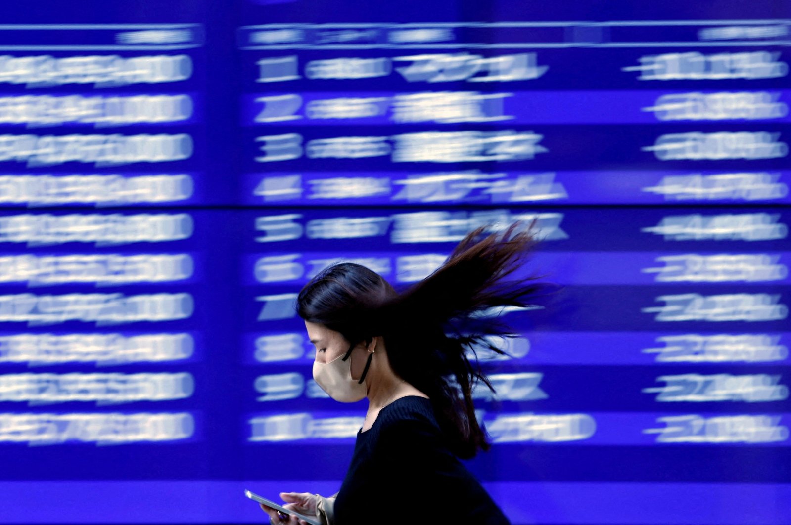 A passerby walks past an electric monitor displaying recent movements of various stock prices outside a bank in Tokyo, Japan, March 22, 2023. (Reuters Photo)