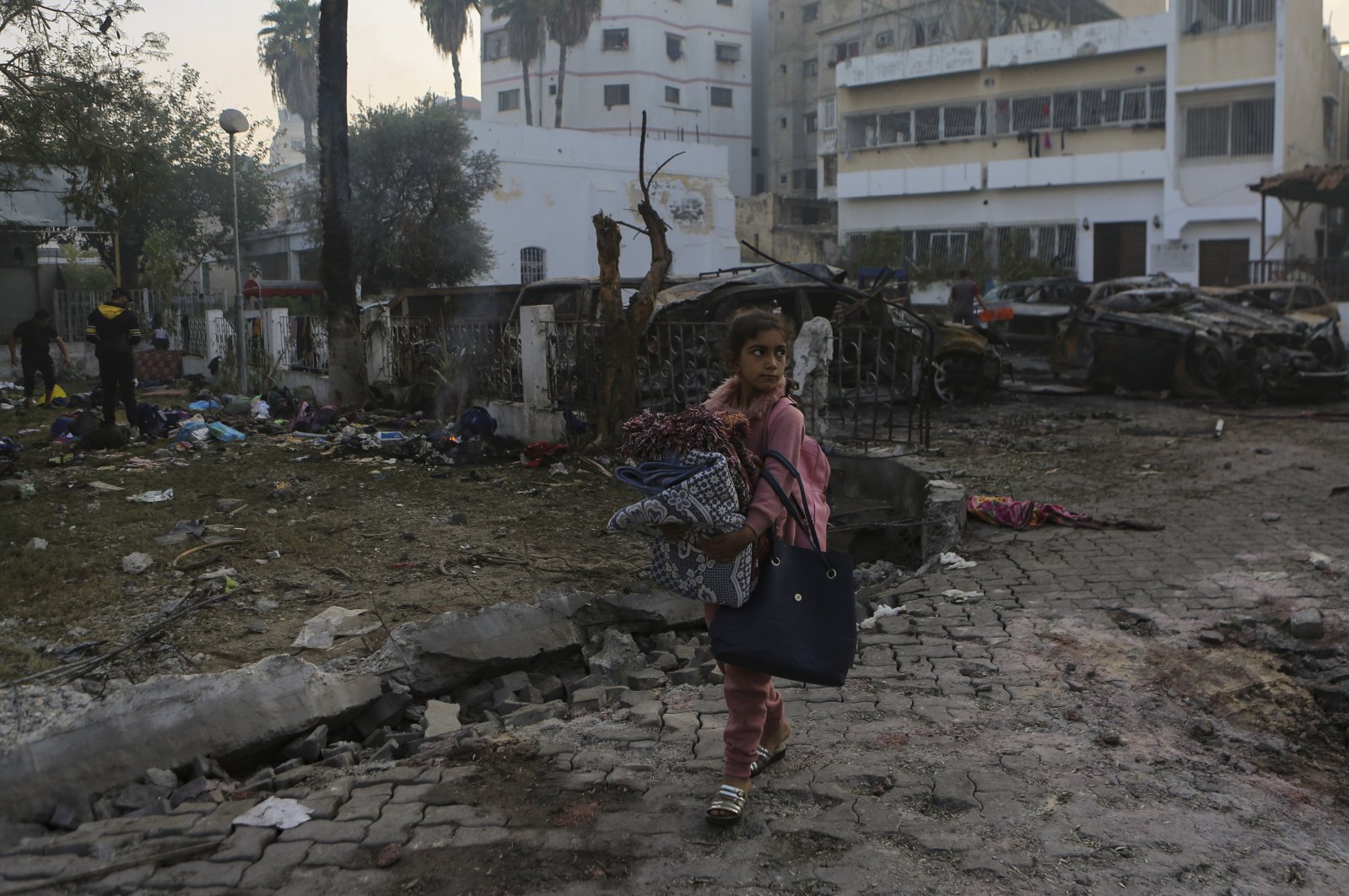 A Palestinian girl carries a blanket as she walks past the site of a deadly airstrike at al-Ahli Baptist Hospital, in Gaza City, Palestine, Oct. 18, 2023. (AP Photo)