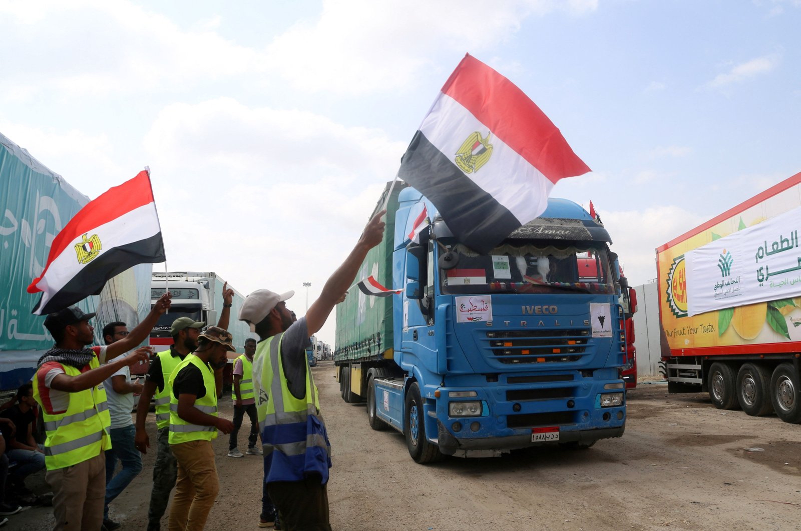 People on the Egyptian side of the Rafah border crossing wave flags as a convoy of lorries carrying humanitarian aid crosses to the Gaza Strip, Palestine, Oct. 22, 2023. (AFP Photo)