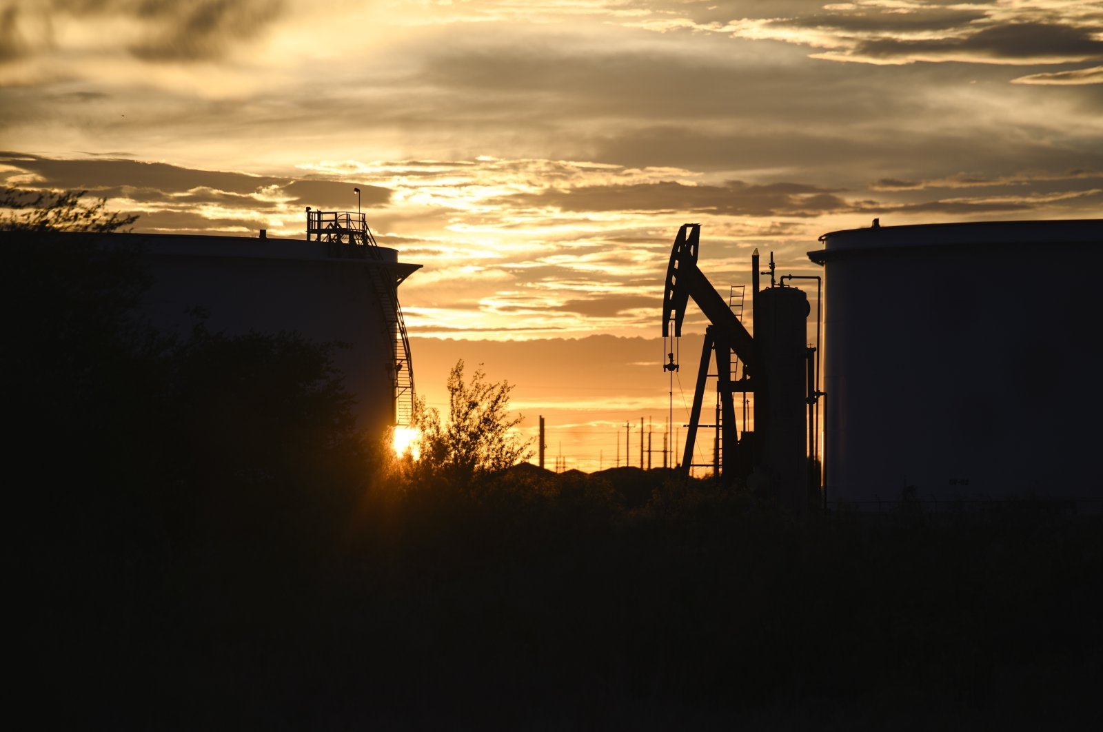 The sun begins to set behind crude oil tanks and a pumpjack, in Midland, Texas, U.S., July 5, 2022. (AP Photo)