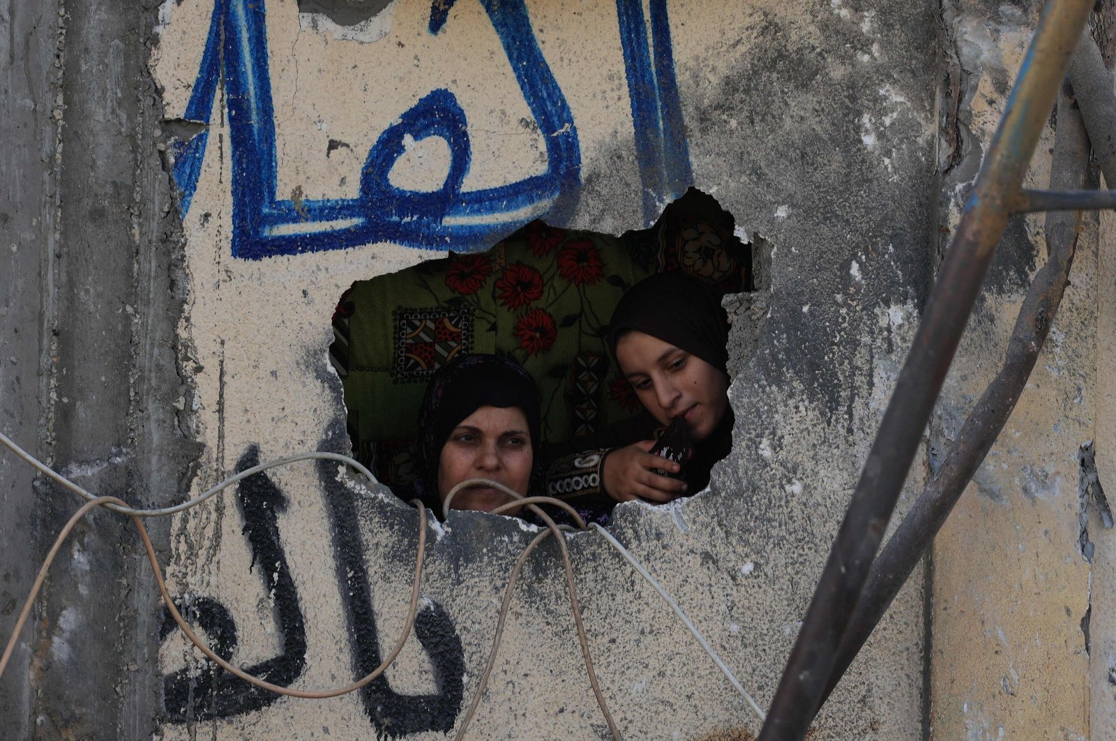 Palestinian women look out from a hole in a damaged wall following Israeli strikes on the Rafah refugee camp in the southern Gaza Strip, Palestine, Oct. 25, 2023. (AFP Photo)