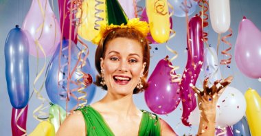 A woman throws a handful of confetti at a nostalgic 1960s party decorated with streamers and balloons. (Getty Images Photo)