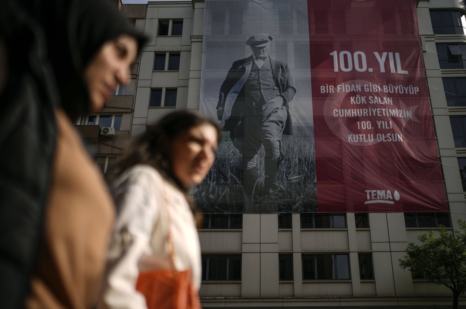 Two women pass by a poster in the backdrop showing an image of the Republic of Türkiye&#039;s founder Mustafa Kemal Atatürk, to commemorate the 100-year anniversary of the Republic, in Istanbul, Türkiye, Oct. 25, 2023. (AP Photo)