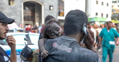 A Palestinian man covered in dust carries a baby girl into the Al-Shifa hopsital in Gaza City following Israeli strikes, Palestine, Oct. 29, 2023. (AFP Photo)