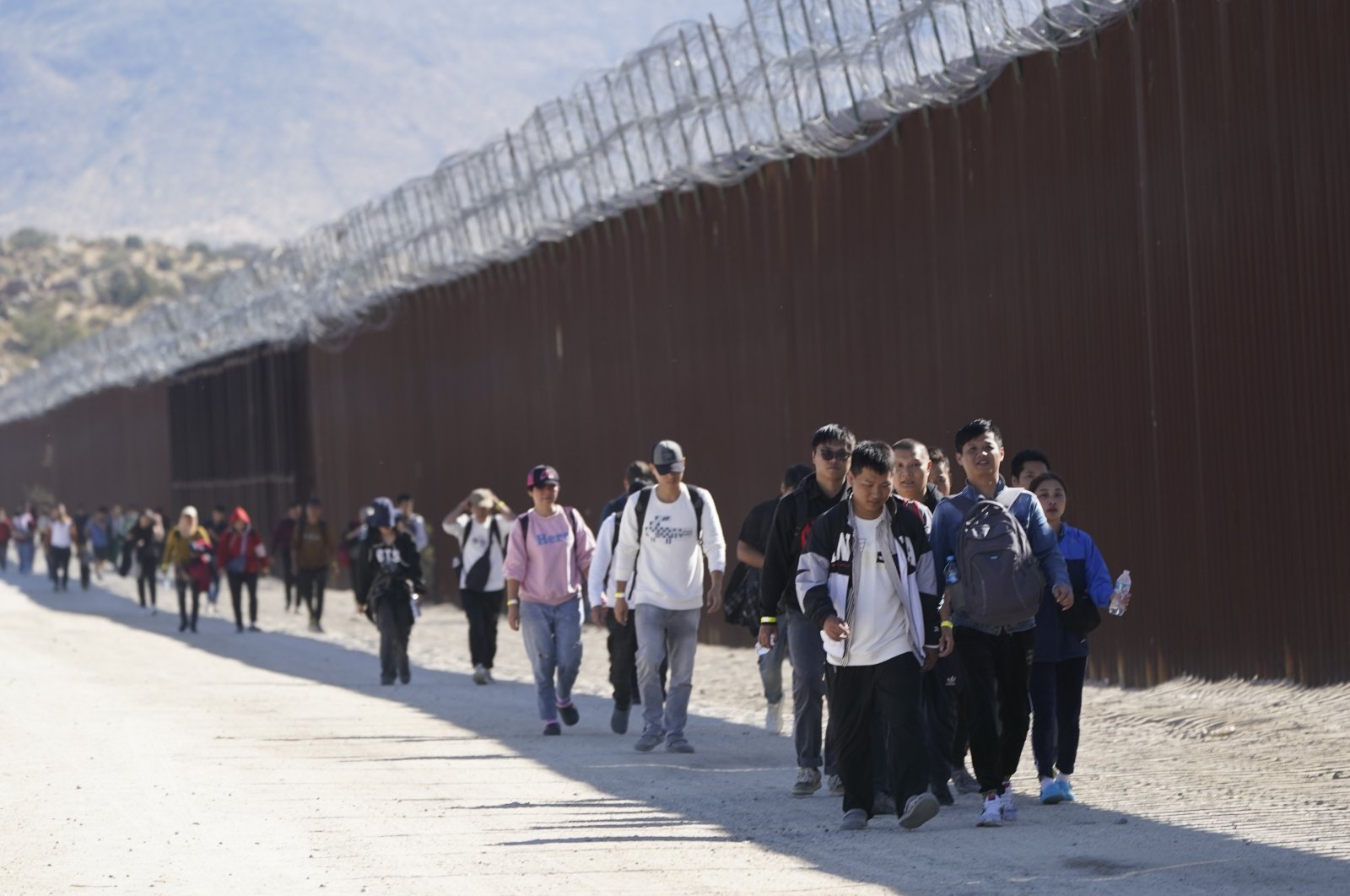 A group of people, including many from China, walk along the wall after crossing the border with Mexico to seek asylum, near Jacumba, California, U.S., Oct. 24, 2023. (AP Photo)