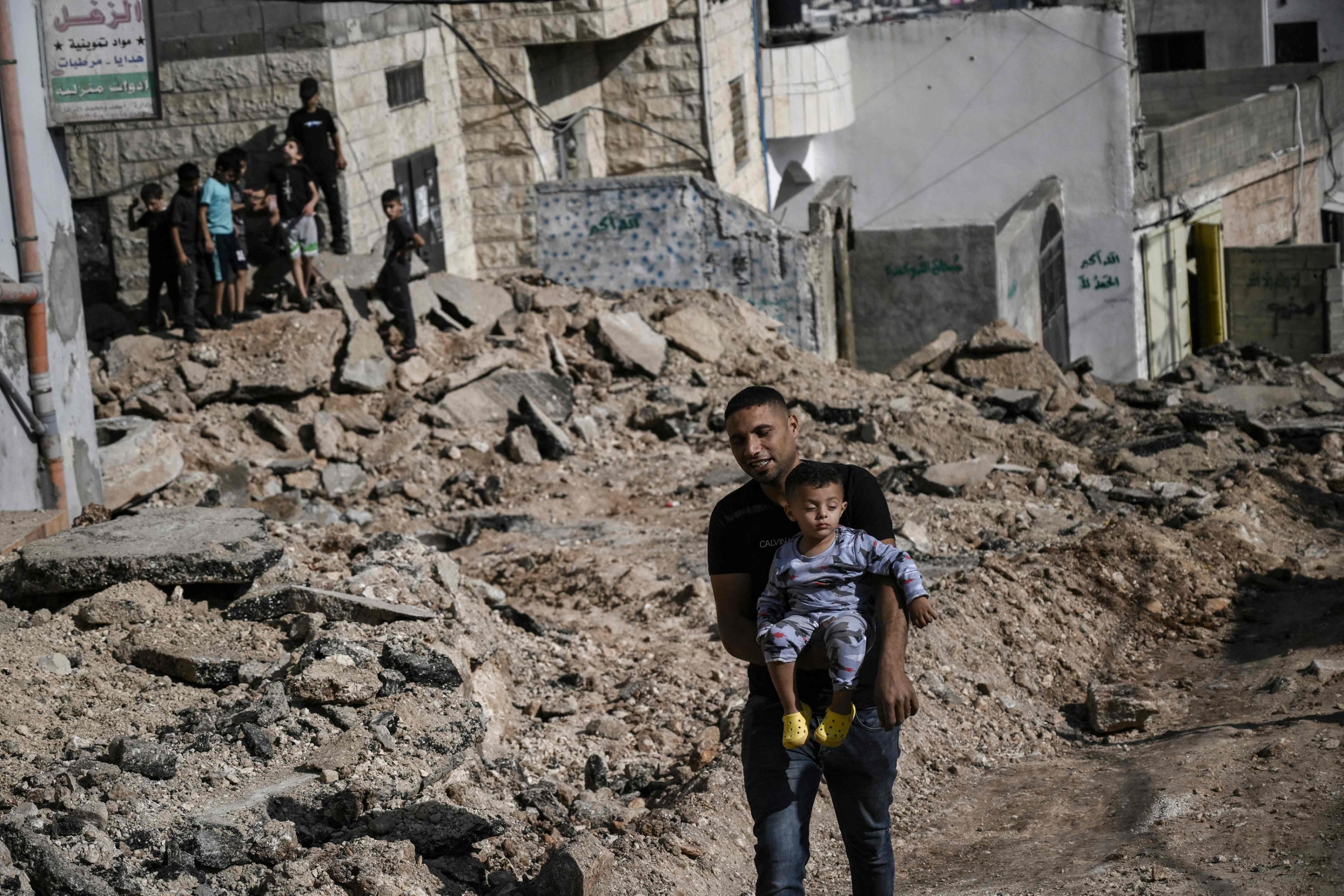 A Palestinian man carries his child as he walks along a road ripped up by an Israeli manned bulldozer during their incursion in the Palestinian Jenin refugee camp, Jenin, occupied West Bank, Nov. 3, 2023. (AFP Photo)