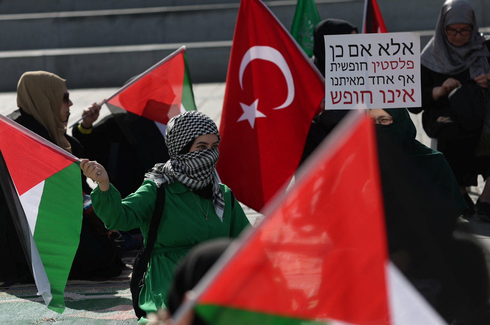 Women holding Turkish and Palestinian flags take part in a sit-in protest in support of Palestinians in Gaza with a sign in Hebrew that reads, &quot;Unless Palestine is free, none of us are free,&quot; in Istanbul, Türkiye, Oct. 22, 2023. (Reuters Photo)