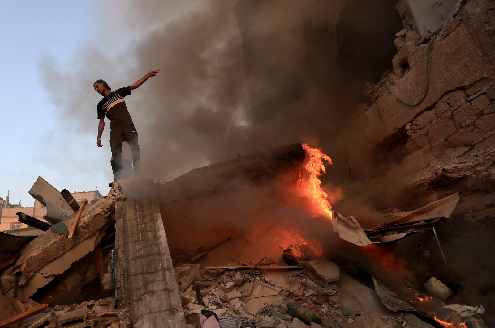A Palestinian man gestures as he stands on the rubble of a collapsed building as a fire burns following a strike by the Israeli military on Khan Yunis in the southern Gaza Strip, Palestine, Nov. 4 , 2023, (AFP Photo)