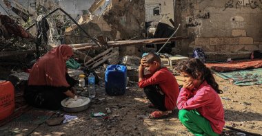 Nesrine, a Palestinian woman, mixes flour with water to make bread as children watch, amid the ruins of the family home destroyed in an Israeli strike in Rafah, southern Gaza, Palestine, Nov. 7, 2023. (AFP Photo)