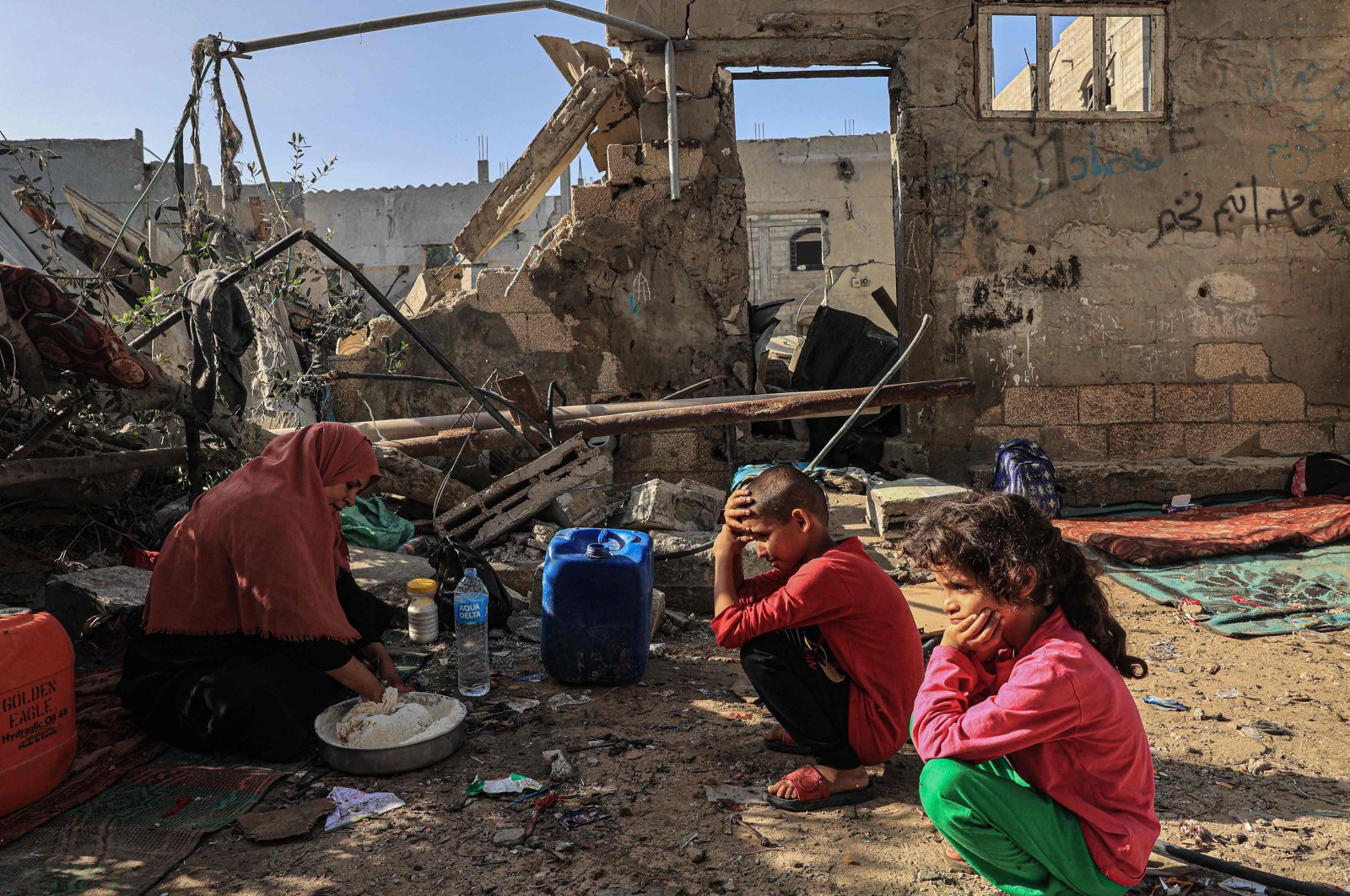 Nesrine, a Palestinian woman, mixes flour with water to make bread as children watch, amid the ruins of the family home destroyed in an Israeli strike in Rafah, southern Gaza, Palestine, Nov. 7, 2023. (AFP Photo)