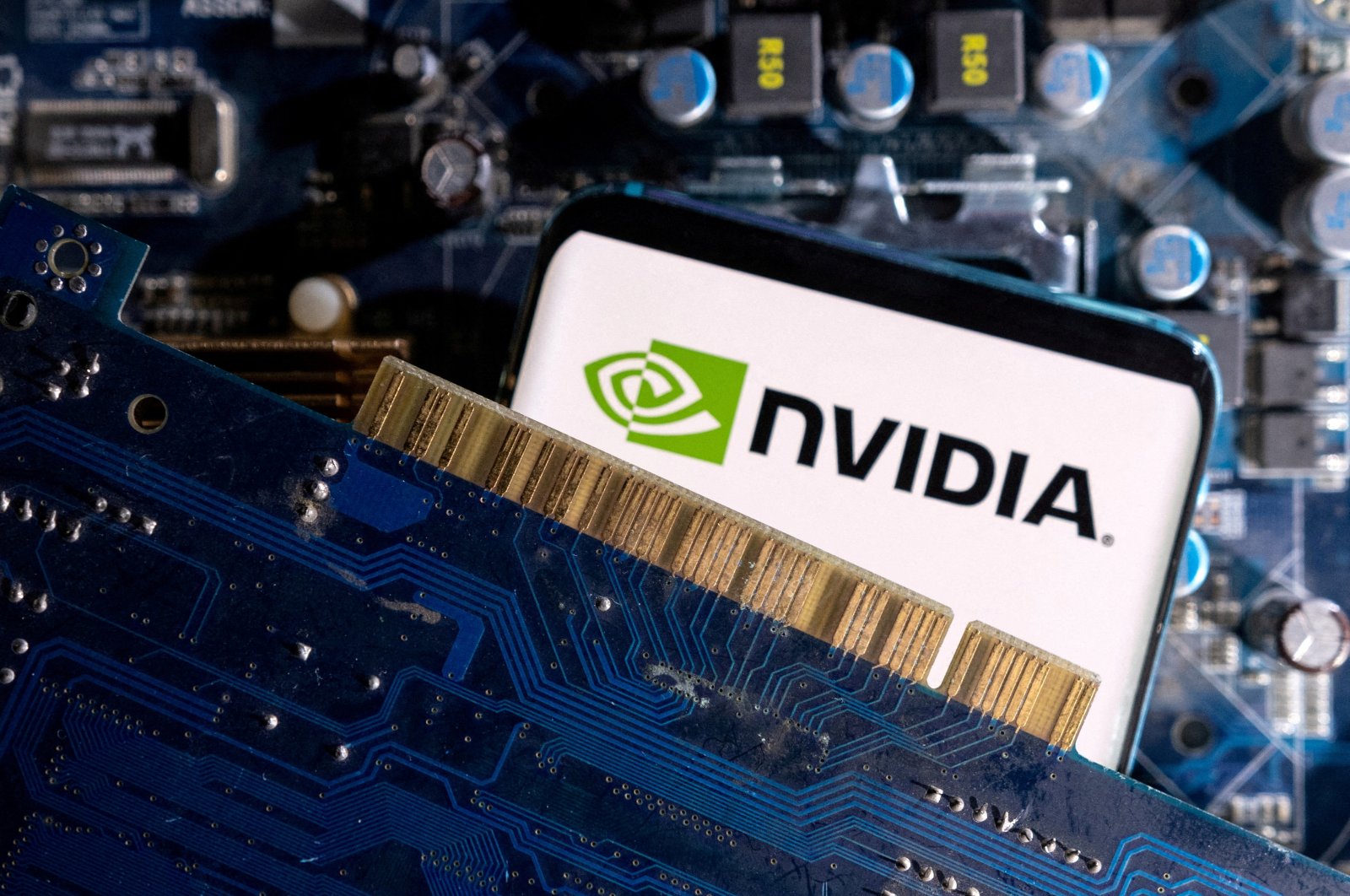 A smartphone with a displayed NVIDIA logo is placed on a computer motherboard in this illustration taken, March 6, 2023. (Reuters Photo)