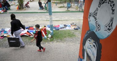 People pass by used clothes for barter or sale on a sidewalk in Villa Fiorito, Lomas de Zamora where a pedestrian bridge is decorated with portraits of late Argentine football star Diego Maradona, Argentina, Nov. 13, 2023. (AFP Photo)
