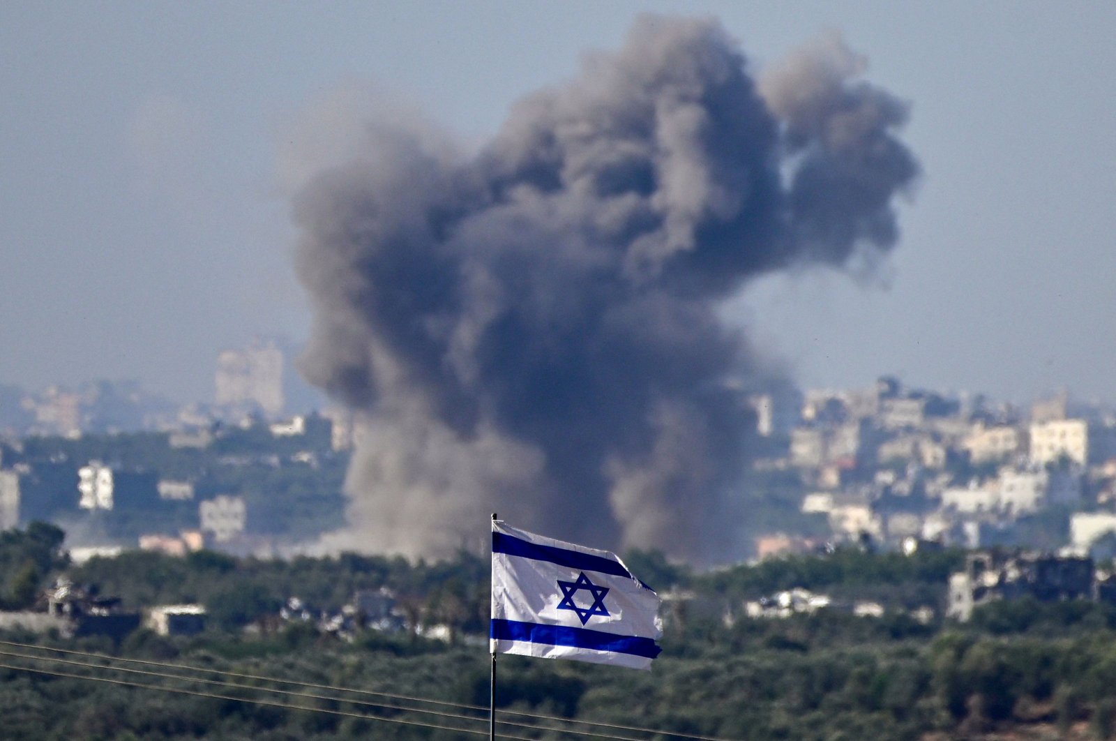 This picture taken from the border with the Gaza Strip shows a national flag on the Israeli side as smoke billows during an Israeli strike on the Palestinian territory on Nov. 21, 2023. (AFP Photo)