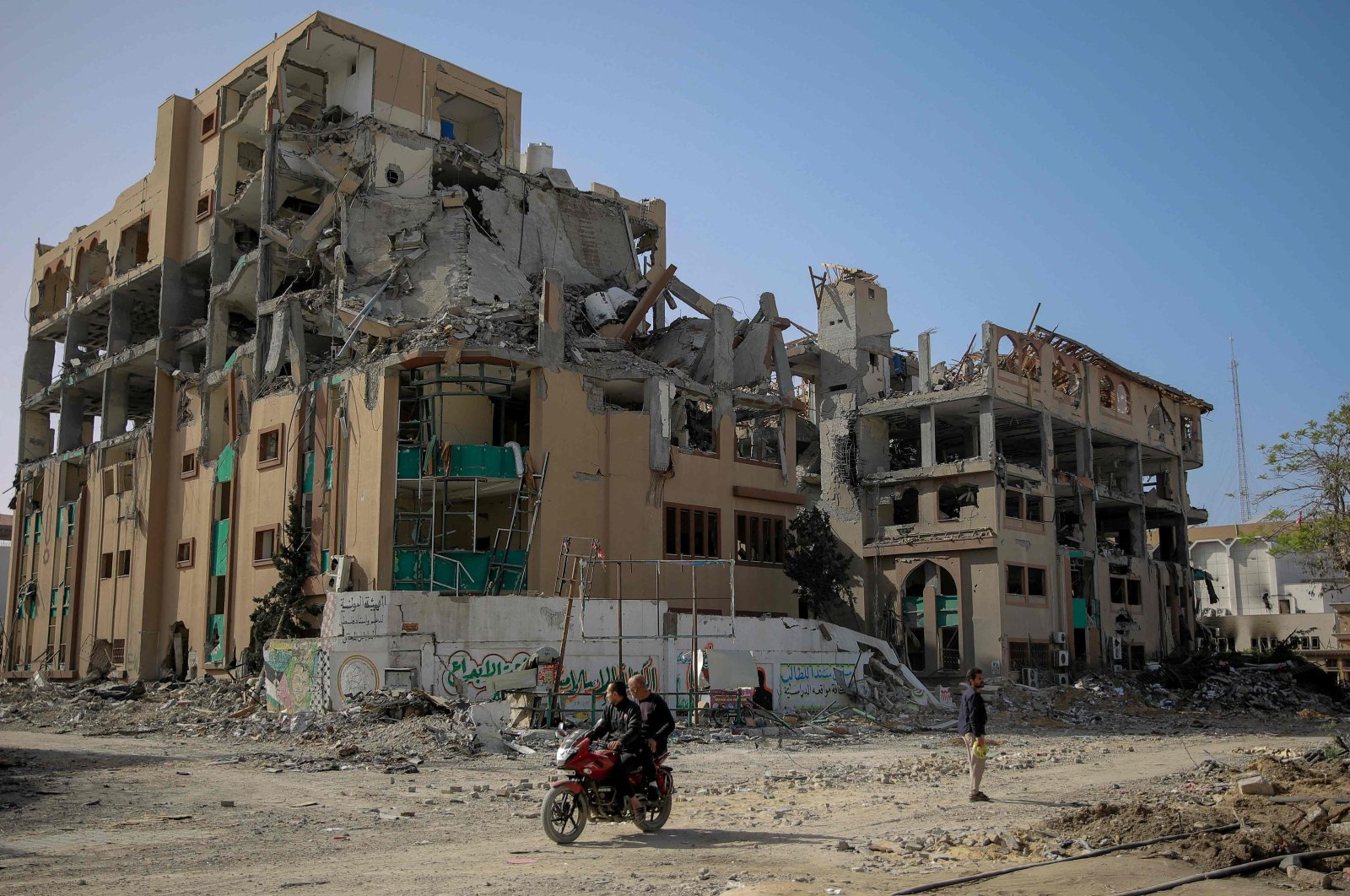 Palestinians drive a motorcycle past the destroyed building of the Islamic University in Gaza City, Palestine, Nov. 26, 2023. (AFP Photo)