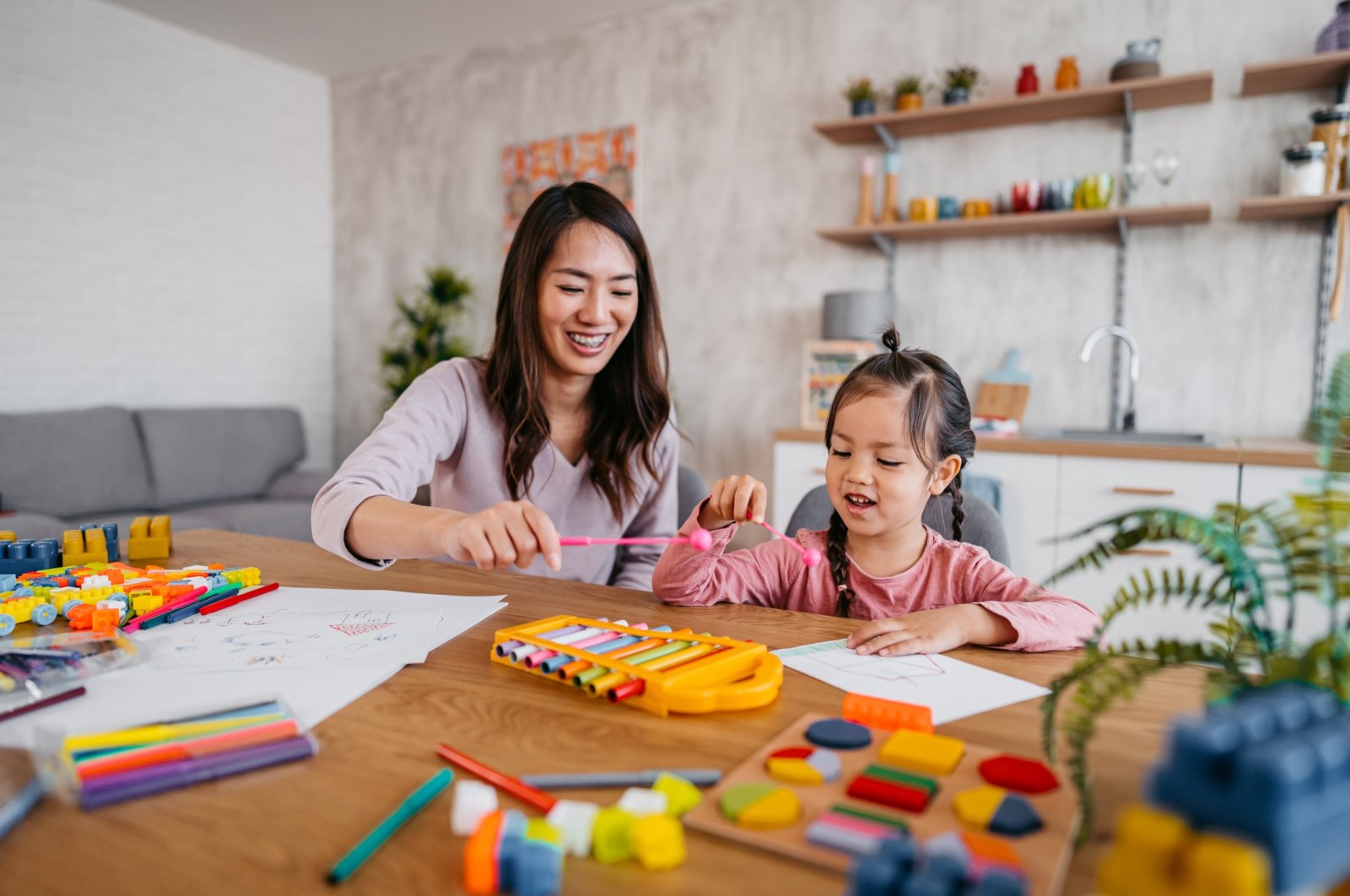 A young mother playing with her child at the kitchen table with toys, April 4, 2023. (Getty Images Photo)