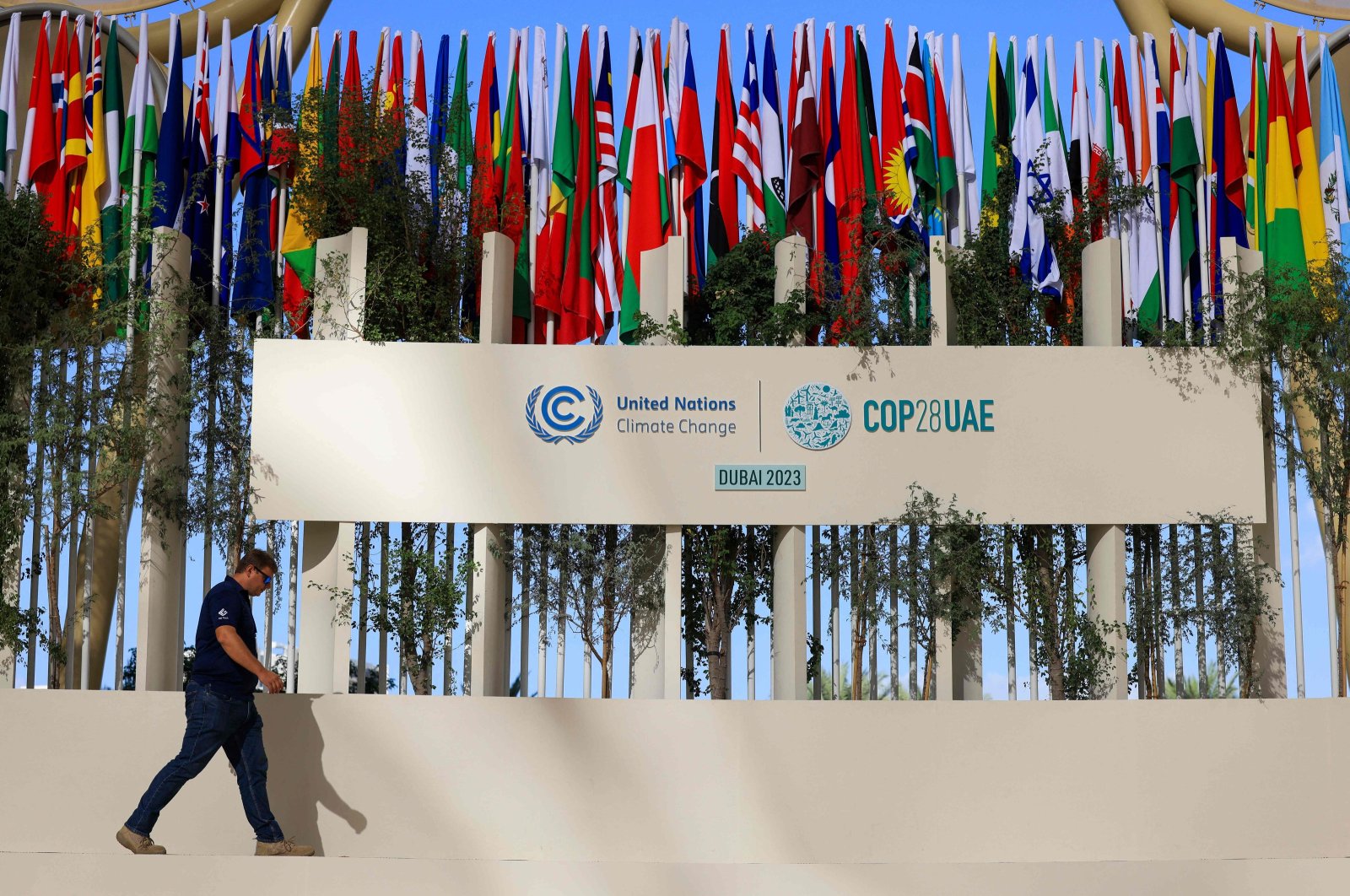 A man walks past national flags of participating countries at the venue of the COP28 United Nations climate summit in Dubai, United Arab Emirates (UAE), Nov. 30, 2023. (AFP Photo)