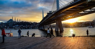 People walk next to Bosporus Strait's Golden Horn at sunset while the metro bridge is seen in the background in Istanbul, Türkiye, Jan. 18, 2020. (AFP Photo)