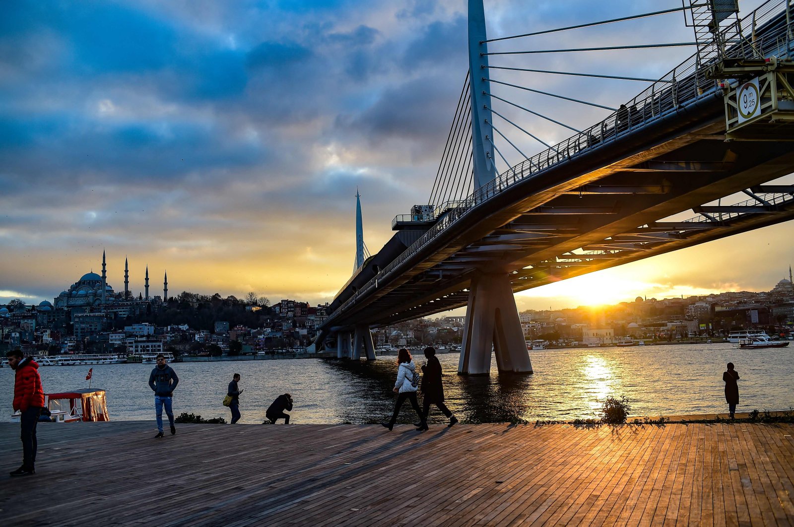 People walk next to Bosporus Strait&#039;s Golden Horn at sunset while the metro bridge is seen in the background in Istanbul, Türkiye, Jan. 18, 2020. (AFP Photo)