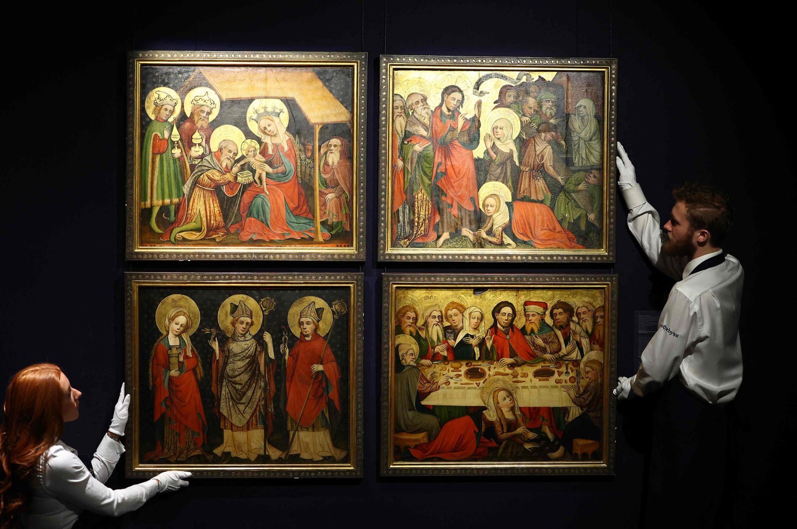 Gallery assistants hold four works by The Master of the Hildesheim Magdalene Legend, Four panels from the Hildesheim Magdalene Altarpiece, tempera and oil on oak panels, at a press preview in London, U.K., Dec.1, 2023. (AFP Photo)