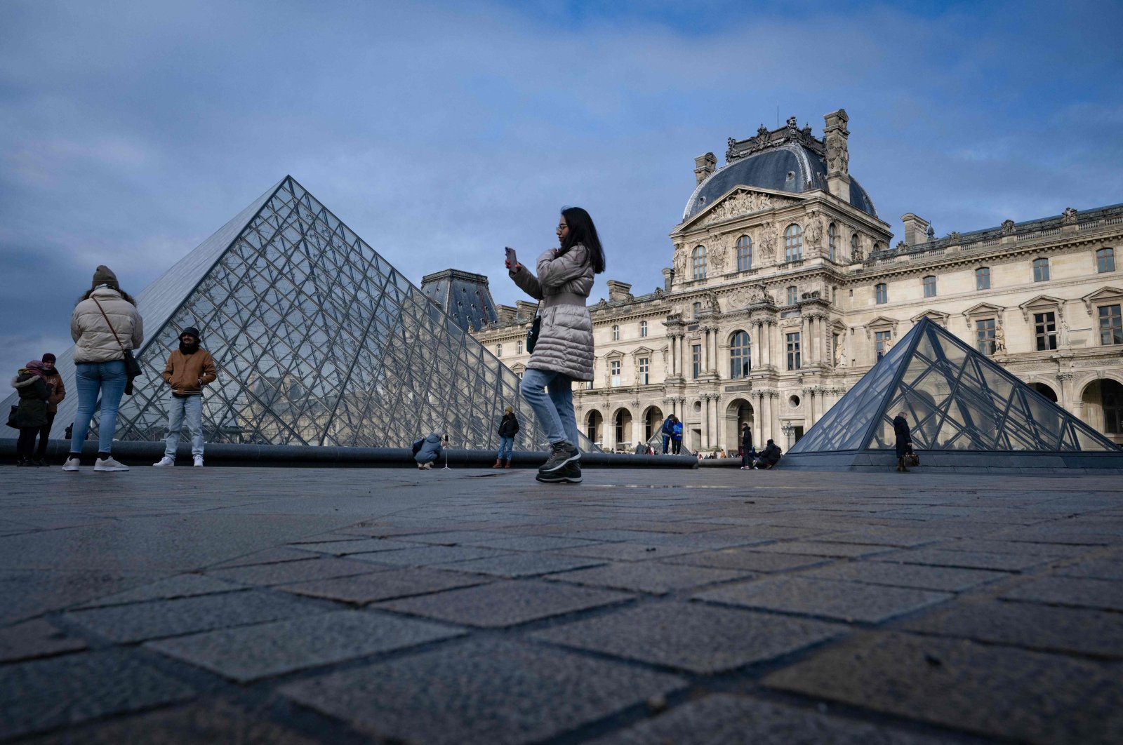 A tourist takes a picture at the Cour Napoleon in front of the Louvre Pyramid, designed by Chinese-American architect Ieoh Ming Pei, standing at the Louvre museum, in central Paris, France, Dec. 4, 2023. (AFP Photo)