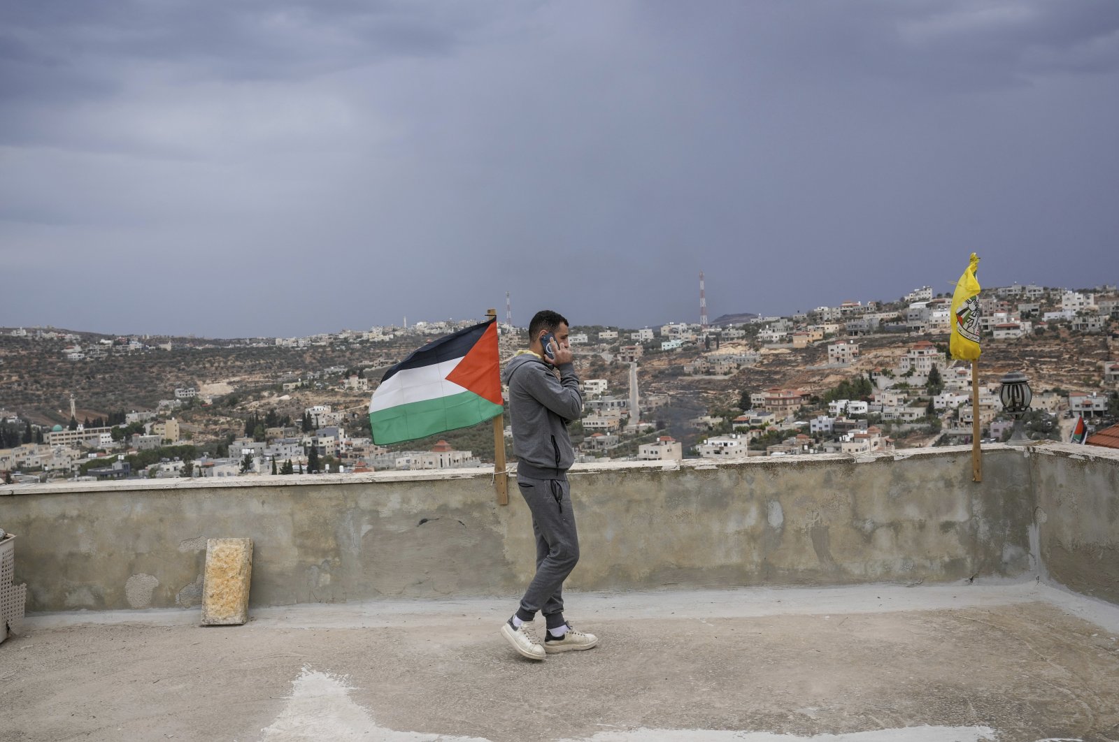 The son of Abdelazim Wadi, whose uncle and cousin were killed by Israeli settlers during a funeral procession on Oct. 12, takes a phone call from the roof of his home beside the Palestinian flag and the flag of the Fatah in the rural Palestinian village of Qusra, West Bank, Nov. 12, 2023. (AP Photo)