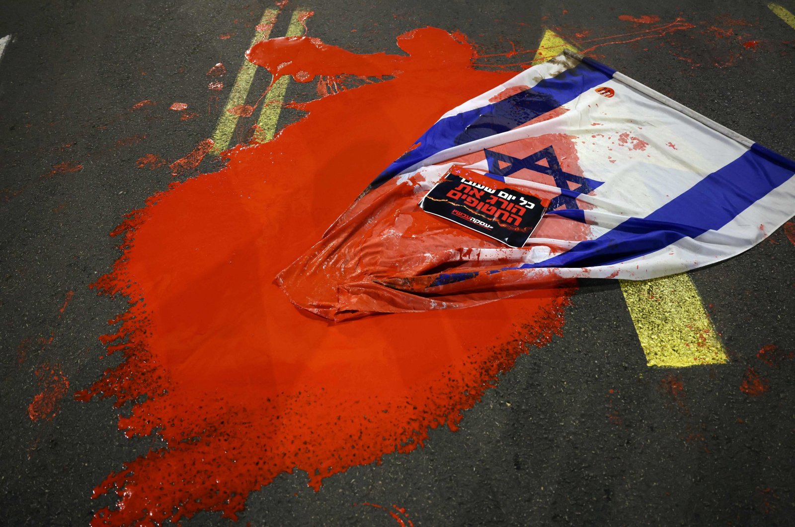 An Israeli flag is covered in red paint as relatives and supporters of hostages held in Gaza demonstrate outside the Israeli Defense Ministry, Tel Aviv, Israel, Dec. 15, 2023. (AFP Photo)