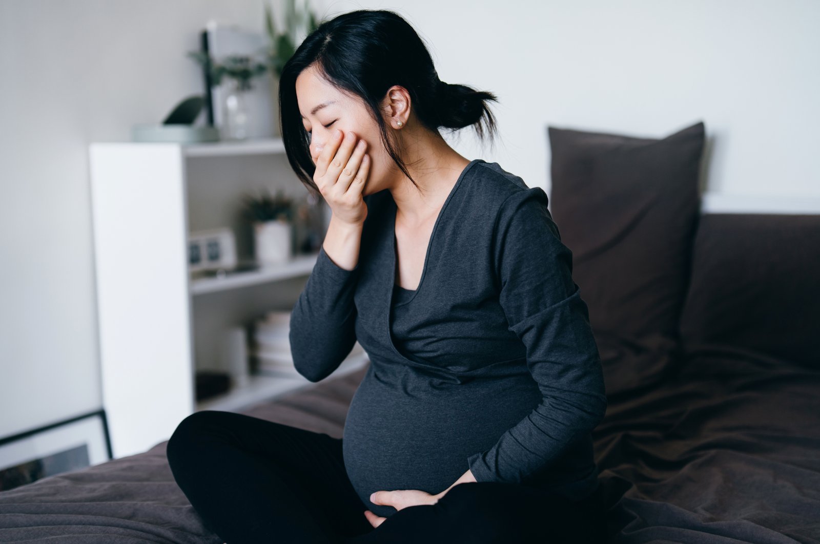 A young pregnant woman sitting on her bed, feeling nauseous and covering her mouth, suffering from morning sickness in this undated file photo. (Getty Images)