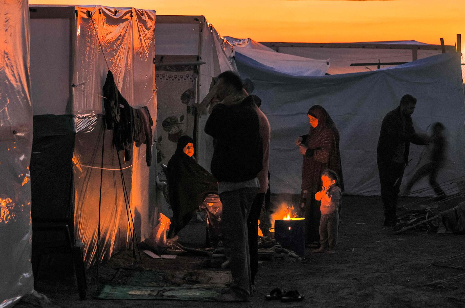 Men pray at sunset as people sit by a fire outside one of the tents housing Palestinians displaced by Israel&#039;s ruthless attacks on Gaza Strip, Dec.18, 2023. (AFP Photo)