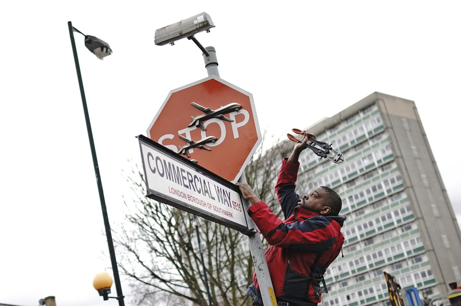 A person removes a piece of artwork by Banksy, which shows what looks like three drones on a traffic stop sign, London, U.K., Dec. 22, 2023. (AP Photo)