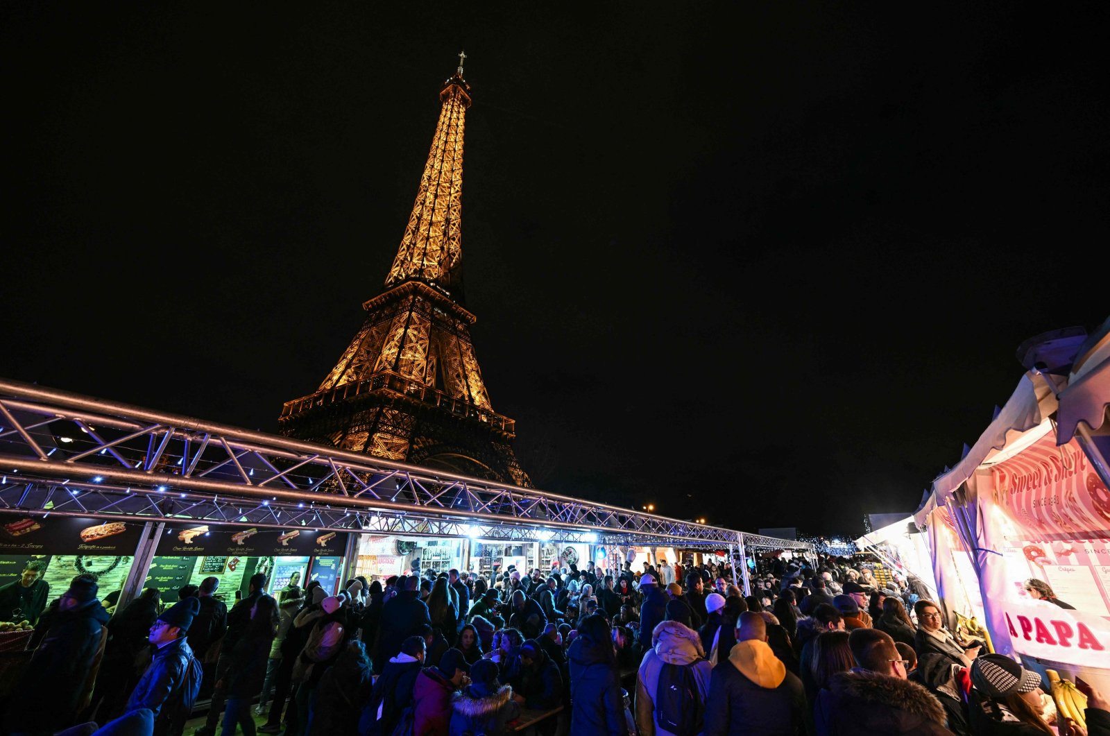 This photograph shows a view of visitors in a Christmas market with the Eiffel Tower monument in the background, in Paris, France, Dec. 23, 2023. (AFP Photo)
