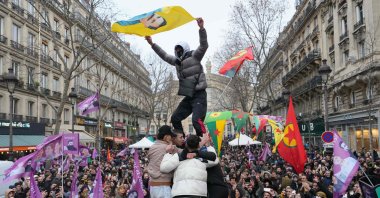 A man waves a banner bearing a portrait of Abdullah Öcalan (C), the jailed leader of the terrorist group PKK, as he is lifted in the air during a rally to mark the anniversary of the Enghien Street killing, Paris, France, Jan. 6, 2024. (AFP Photo)