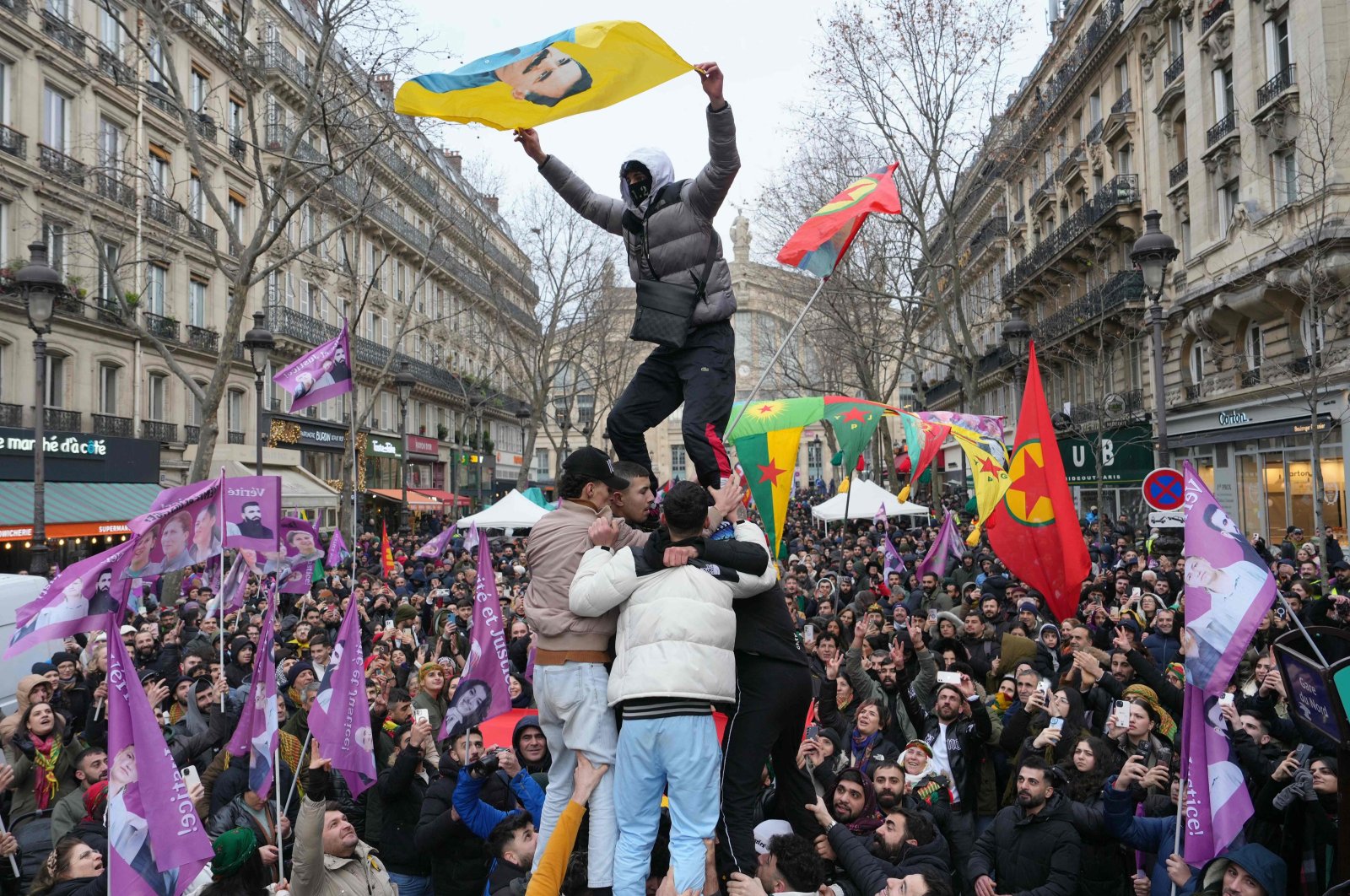 A man waves a banner bearing a portrait of Abdullah Öcalan (C), the jailed leader of the terrorist group PKK, as he is lifted in the air during a rally to mark the anniversary of the Enghien Street killing, Paris, France, Jan. 6, 2024. (AFP Photo)