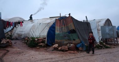 A young boy walks in front of tents on a cold and rainy day, at a camp for displaced Syrians in Idlib, Syria, Jan. 10, 2024. (AFP Photo)