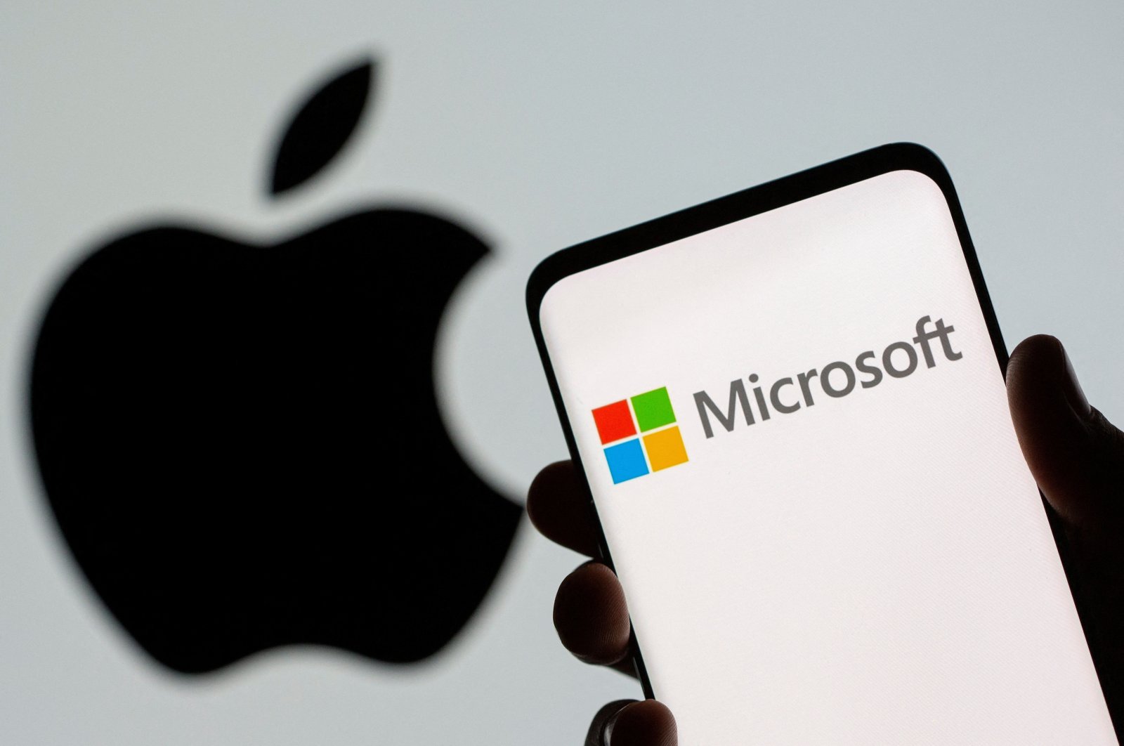 The Microsoft logo is seen on the smartphone in front of an Apple logo in this illustration taken on July 26, 2021. (Reuters Photo)