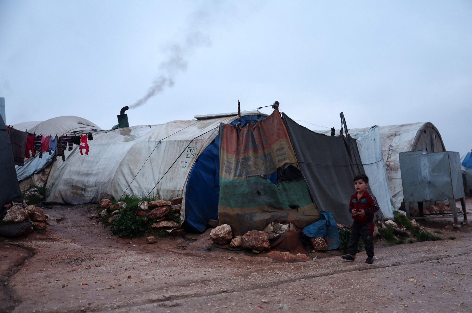 A young boy walks in front of tents on a cold and rainy day, at a camp for displaced Syrians in Idlib, Syria, Jan. 10, 2024. (AFP Photo)