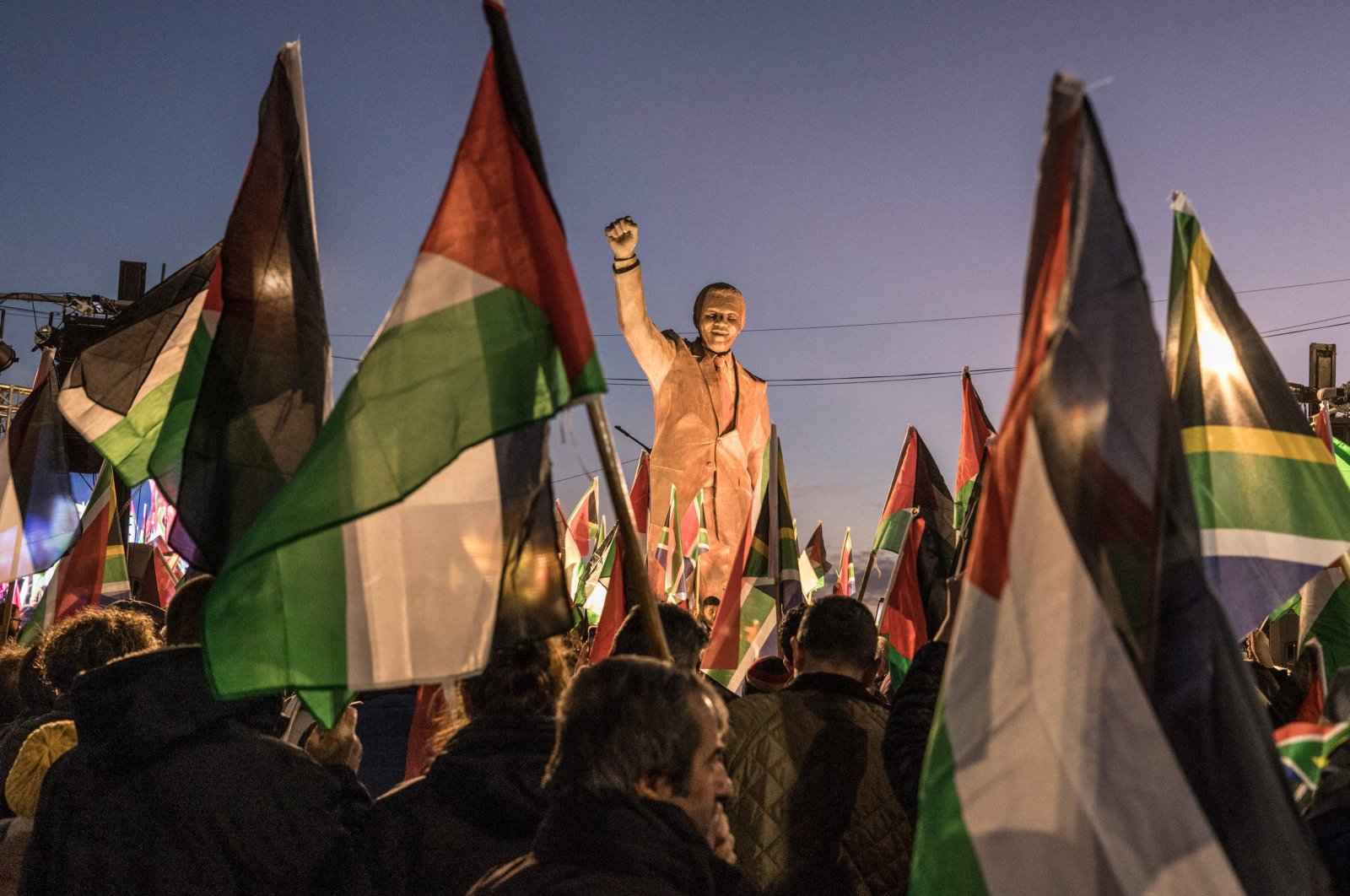 People raise flags and placards as they gather around a statue of late South African President Nelson Mandela to celebrate a landmark genocide case filed by South Africa against Israel at the International Court of Justice, in the occupied West Bank city of Ramallah, Palestine, Jan. 10, 2024.  (AFP Photo)