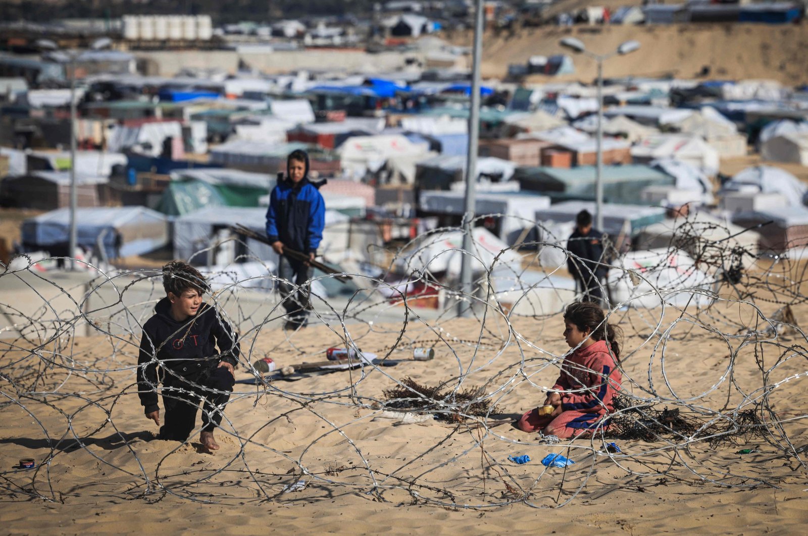 Displaced Palestinian children play behind barbed wire overlooking a makeshift camp on the Egyptian border, Rafah, southern Gaza Strip, Jan. 14, 2024. (AFP Photo)