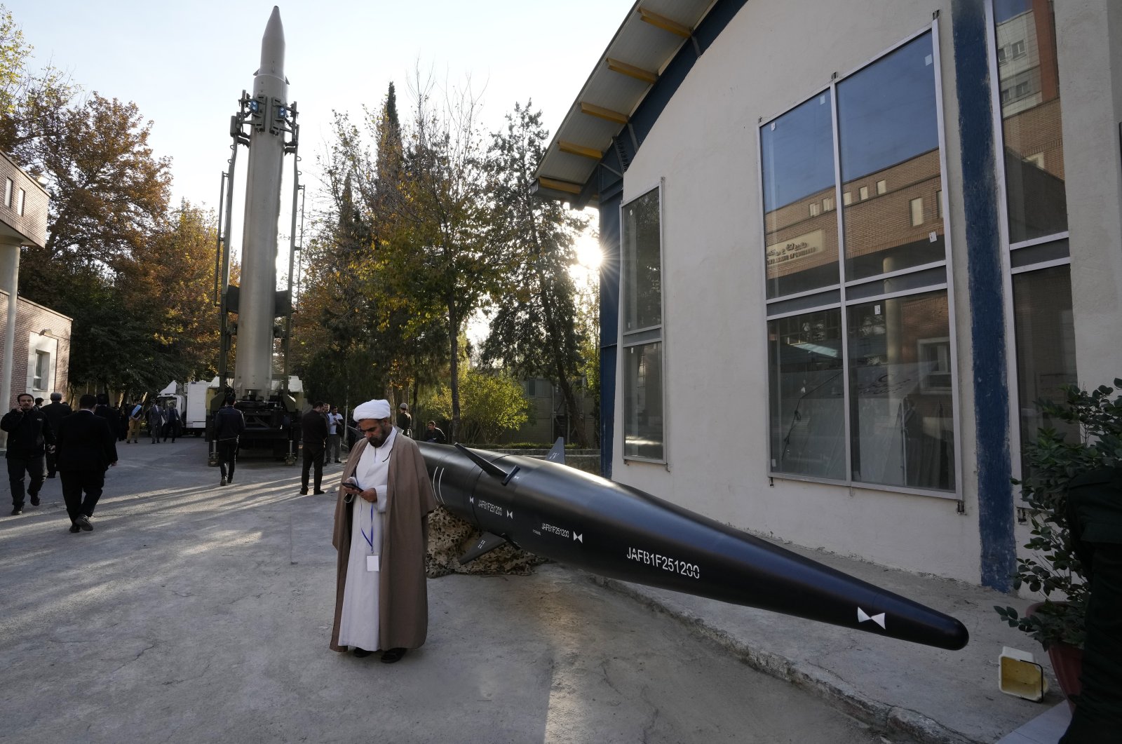 An Iranian cleric uses his cellphone while standing next to missiles displayed in an exhibition during a ceremony in Tehran, Iran, Monday, Nov. 13, 2023. (AP File Photo)