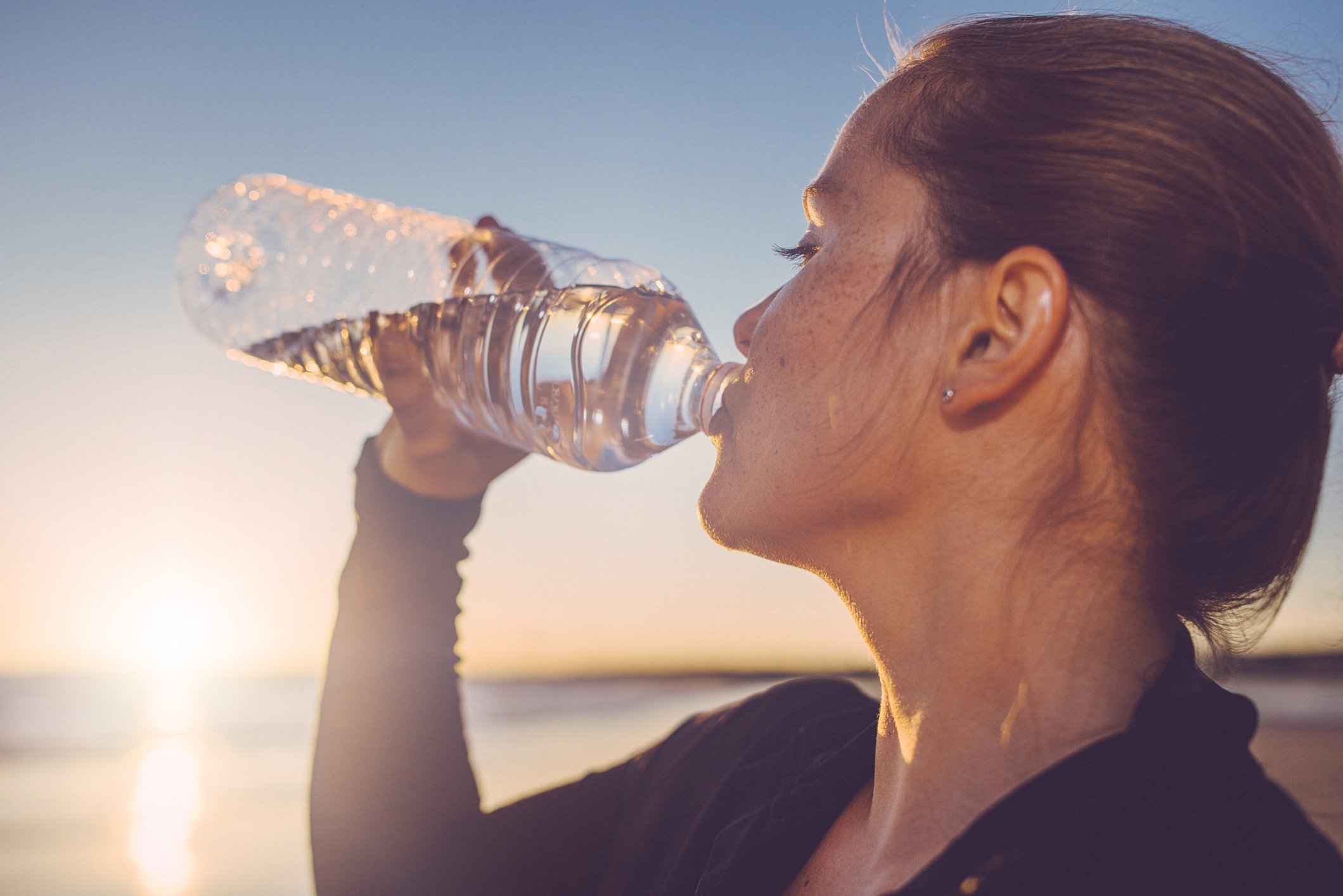 Woman drinking water after running on the beach. (Getty Images Photo)