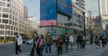 People cross the street beneath a large screen showing the latest stock exchange and economy data in Shanghai, China, Jan. 2, 2024. (EPA Photo)