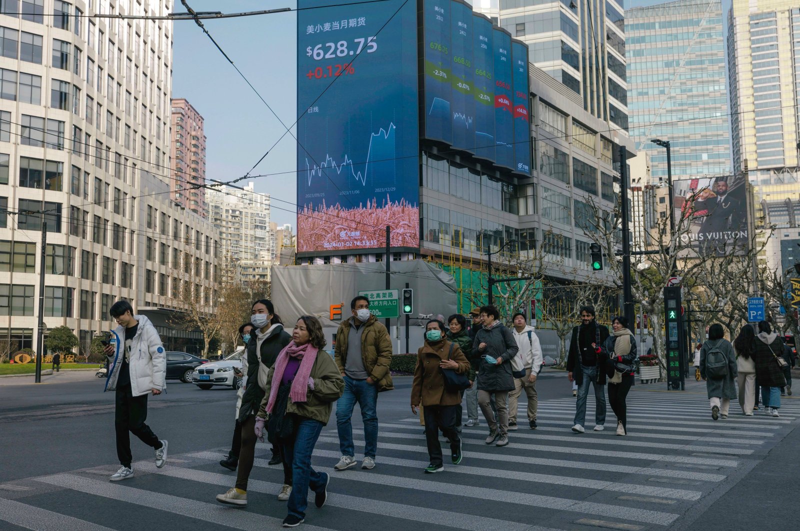 People cross the street beneath a large screen showing the latest stock exchange and economy data in Shanghai, China, Jan. 2, 2024. (EPA Photo)