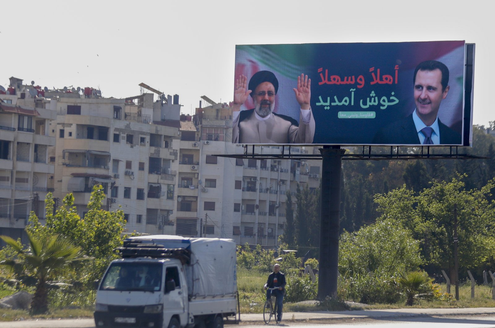 People drive under a poster with pictures of Iranian President Ebrahim Raisi (L) and Syria&#039;s Bashar Assad, in Damascus, Syria, May 3, 2023. (AP Photo)