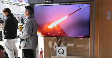 Two men stand next to a television screen showing a news broadcast with file footage of a North Korean missile test, at a railway station, Seoul, South Korea, Feb. 2, 2024. (AFP Photo)