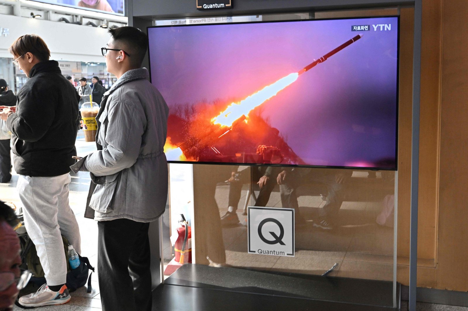 Two men stand next to a television screen showing a news broadcast with file footage of a North Korean missile test, at a railway station, Seoul, South Korea, Feb. 2, 2024. (AFP Photo)