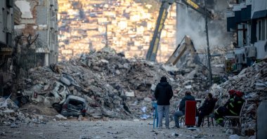 People sit in front of collapsed buildings after the deadly earthquake, in Hatay, southern Türkiye, Feb. 19, 2023. (EPA Photo)