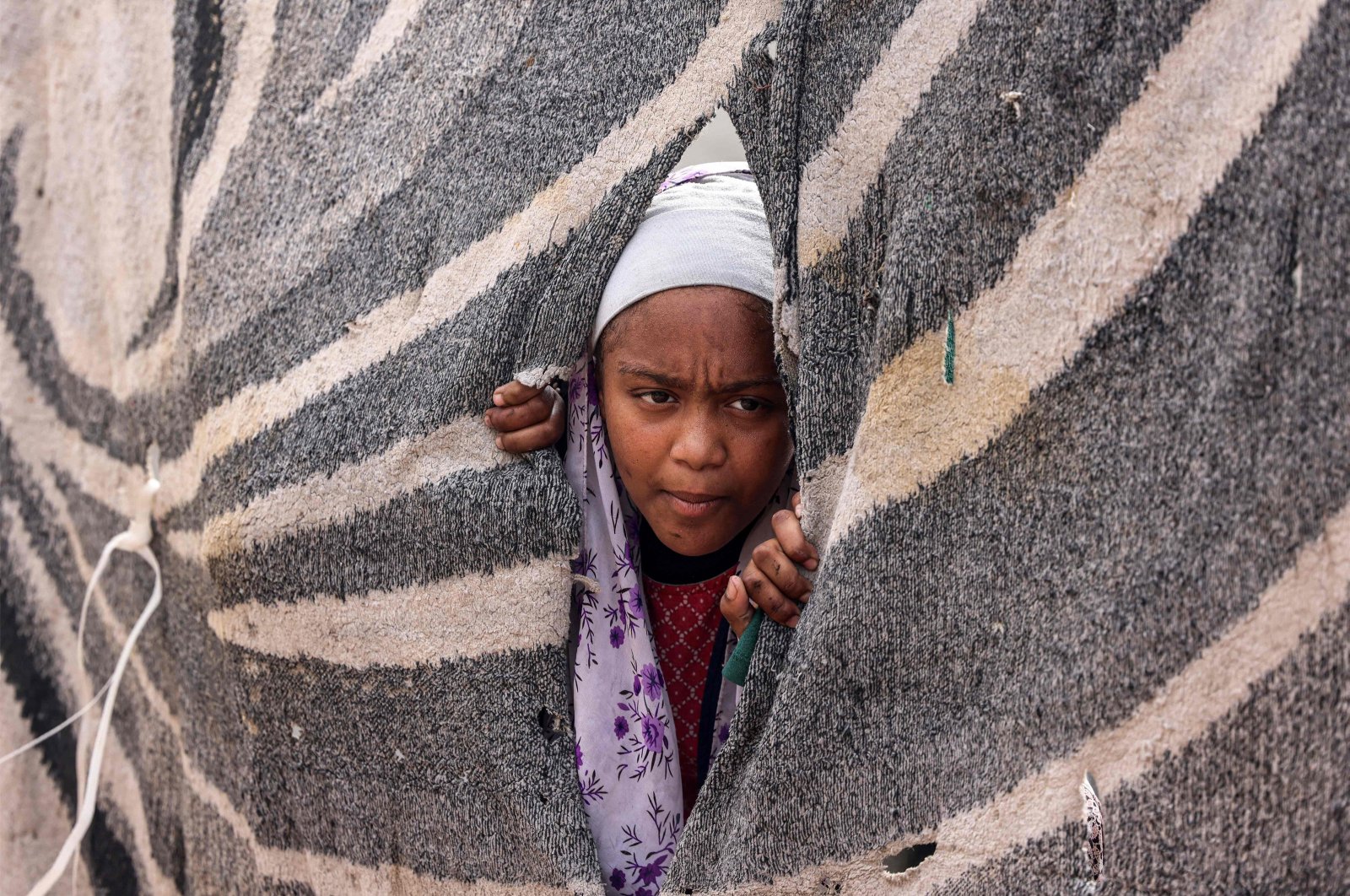 A girl peeks out from a hole in a canvas at a refugee camp in Rafah, southern Gaza Strip, Palestine, Feb. 13, 2024. (AFP Photo)