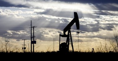 The sun shines through the clouds as it begins to set behind a pumpjack, outside of Goldsmith, Texas, U.S., March 30, 2022. (AP Photo)